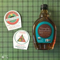 a bottle of maple syrup next to two stickers on a green tablecloth background