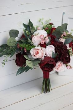 a bouquet of red and pink flowers sitting on top of a wooden table next to a white wall