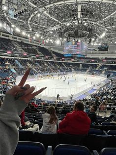 a person holding up their hand in front of an ice hockey rink with people sitting on the seats