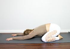 a woman is doing yoga on a mat with her hands behind her head and legs bent forward