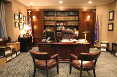 an office with two leather chairs in front of a desk and bookshelves on the wall