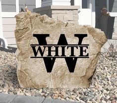 a large rock with the word white on it sitting in front of a house next to some rocks