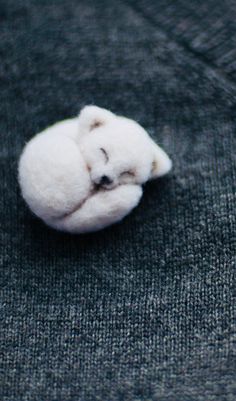 a small white teddy bear laying on top of a gray blanket