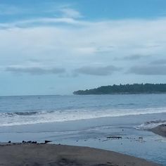 a person walking on the beach with their surfboard in hand and an island in the background