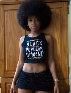 a woman with an afro standing in front of a wooden wall wearing a crop top