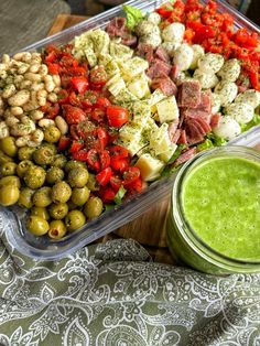 a salad with olives and tomatoes in a plastic container next to a green smoothie