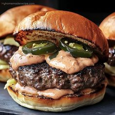 two hamburgers with cheese, onions and peppers on a black plate next to each other