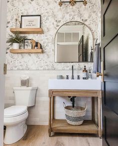 a white toilet sitting next to a bathroom sink under a mirror on top of a wooden shelf