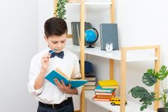 a young boy is reading a book in front of a bookshelf filled with books