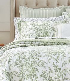 a bed with green and white bedspread, pillows and pillow cases on it