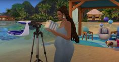 a pregnant woman standing in front of a camera on a tripod next to a body of water