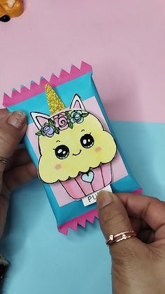 a person holding up a card with a cupcake on it and a unicorn hat on top