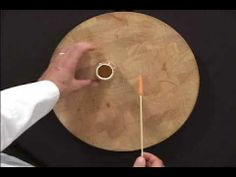 a person is holding an orange object in front of a round wooden board on a black surface