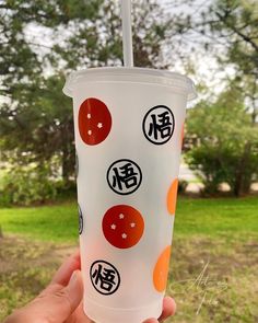 a person holding up a cup with stickers on it in front of some trees