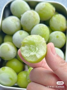 a person holding up a piece of fruit in front of some green grapes and other fruits