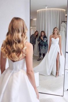 a woman standing in front of a mirror wearing a white dress and looking at her reflection