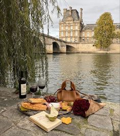 a picnic on the bank of a river with bread, cheese and wine in front of it