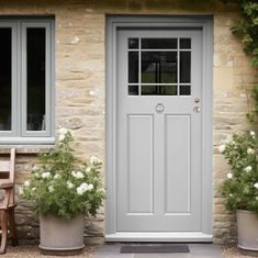 two planters with white flowers in front of a gray door and window on the side of a stone building