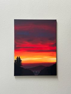 a painting hanging on the side of a wall with a sunset in the sky behind it