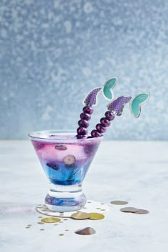 a glass filled with purple liquid and two green butterflies on top of the rims