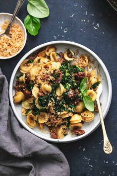 a white bowl filled with pasta and spinach on top of a blue tablecloth