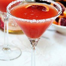 two martini glasses filled with red liquid and garnished with sugar