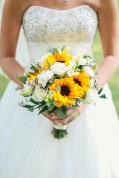 a bride holding a bouquet of sunflowers and roses