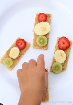 a person reaching for some fruit on top of crackers with kiwis and strawberries