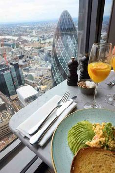 two glasses of orange juice and an avocado toast on a table with a view of the city