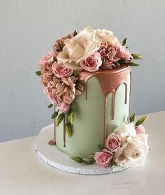 a green cake with pink flowers and dripping icing