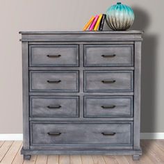 a gray dresser with many drawers on top and a blue vase sitting on top of it