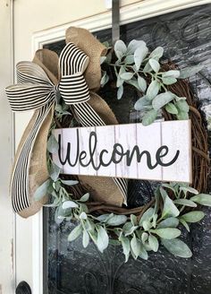 a welcome sign hanging on the front door with greenery and burlock around it