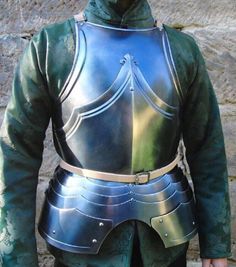 a man in armor standing next to a stone wall with his hands on his hips