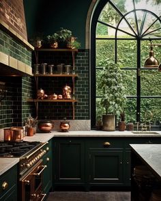 a kitchen with dark green cabinets and copper pots on the stove top, along with an arched window