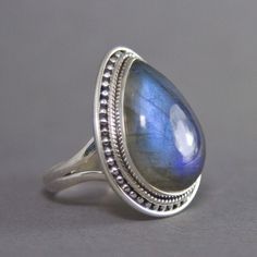 SKU: SS-007Material: 925 stamped sterling silverGemstone(s): Labradorite (N)Gemstone Dimensions: 15 X 22 X 5 mmRing Size: US 7.5Weight: 9.4 gramsThis breathtaking Labradorite cabochon ring is truly a beauty! Set in a classic bezel with a granulated border, the setting enhances the large Labradorite beautifully. The Labradorite not only has a strong blue fire that can be seen from every angle, it also has mica flakes, which add that extra shimmer to an already incredible stone! Silver Teardrop Rings With Spiritual Style, Silver Spiritual Teardrop Ring, Spiritual Silver Teardrop Ring, Silver Teardrop Cabochon Rings, Spiritual Teardrop Gemstone Rings, Teardrop Moonstone Ring In Sterling Silver, Sterling Silver Teardrop Rings Stamped 925, Silver Pear-shaped Moonstone Ring, Sterling Silver Teardrop Rings With Natural Stones