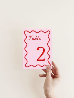 a person holding up a pink card with the number two on it that says table 2