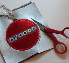 a pair of red scissors sitting on top of a piece of silver paper next to a small patch of fabric