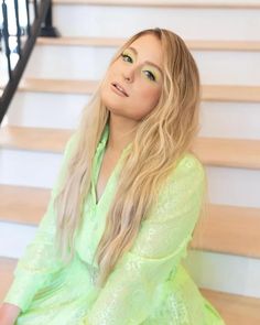 a woman with long blonde hair is sitting on the stairs and posing for a photo