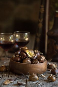 a wooden bowl filled with nuts next to two glasses of wine on top of a table