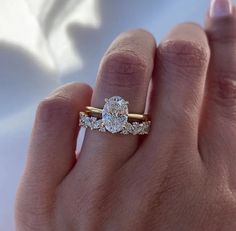 a woman's hand holding a diamond ring with three stones on the band and an oval shaped diamond in the middle