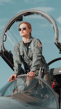 a woman in an air force pilot's uniform sitting on the cockpit of a fighter jet