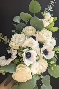 a bouquet of white flowers and greenery on a black background with leaves in the foreground