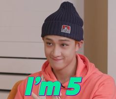 a young man wearing a beanie and looking at the camera with an i'm 5 sign in front of him