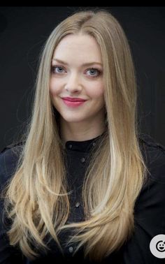 a woman with long blonde hair wearing a black shirt and pink lipstick looks into the camera