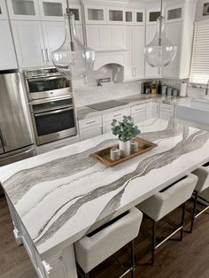 a kitchen with white cabinets and marble counter tops, two vases on the center island