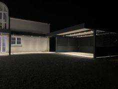 an empty house at night with lights on the windows and dark gravel in front of it