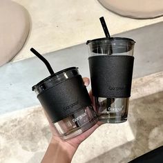 two black tumblers with straws in each one being held by someone's hand