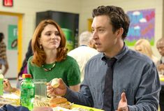 a man and woman sitting at a table with food in front of them, talking to each other