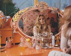 a woman sitting in front of a mirror with lots of glass items on the table