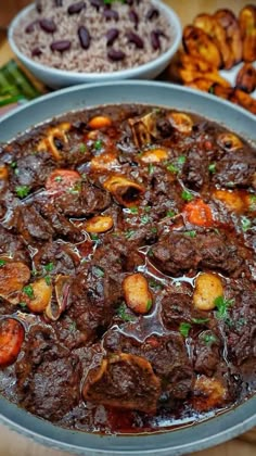 a large bowl filled with meat and vegetables next to other foods on top of a wooden table